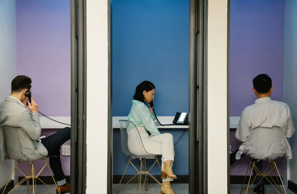 Trois personnes téléphonent chacune dans une cabine individuelle aux parois colorées, dans un bureau partagé